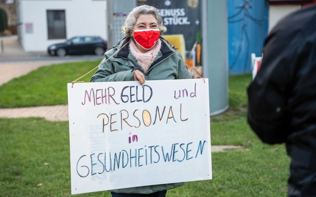 Frau hält ein Schild mit der Aufschrift: Mehr Geld und Personal im Gesundheitswesen